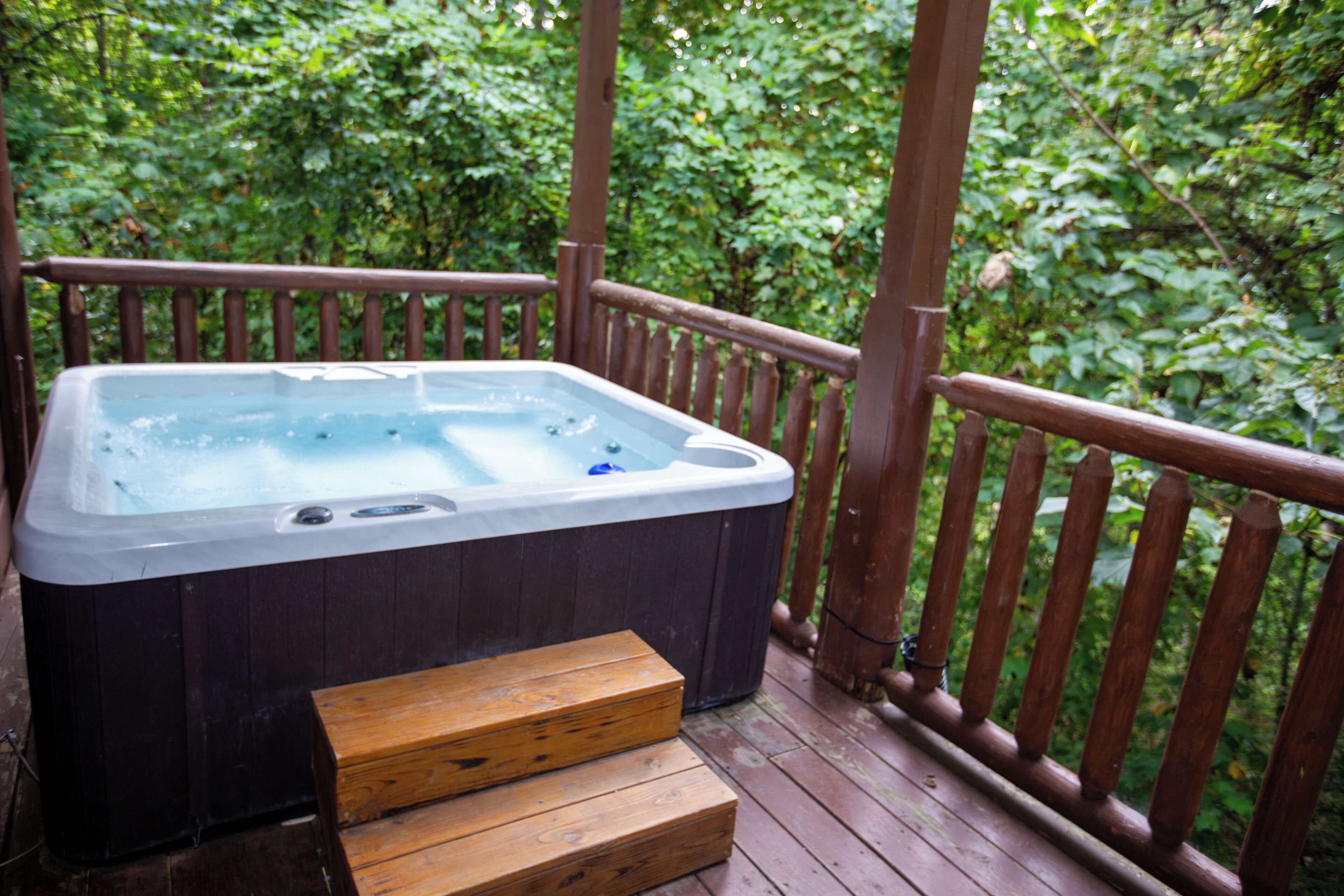 A hot tub on a wooden deck surrounded by lush greenery.