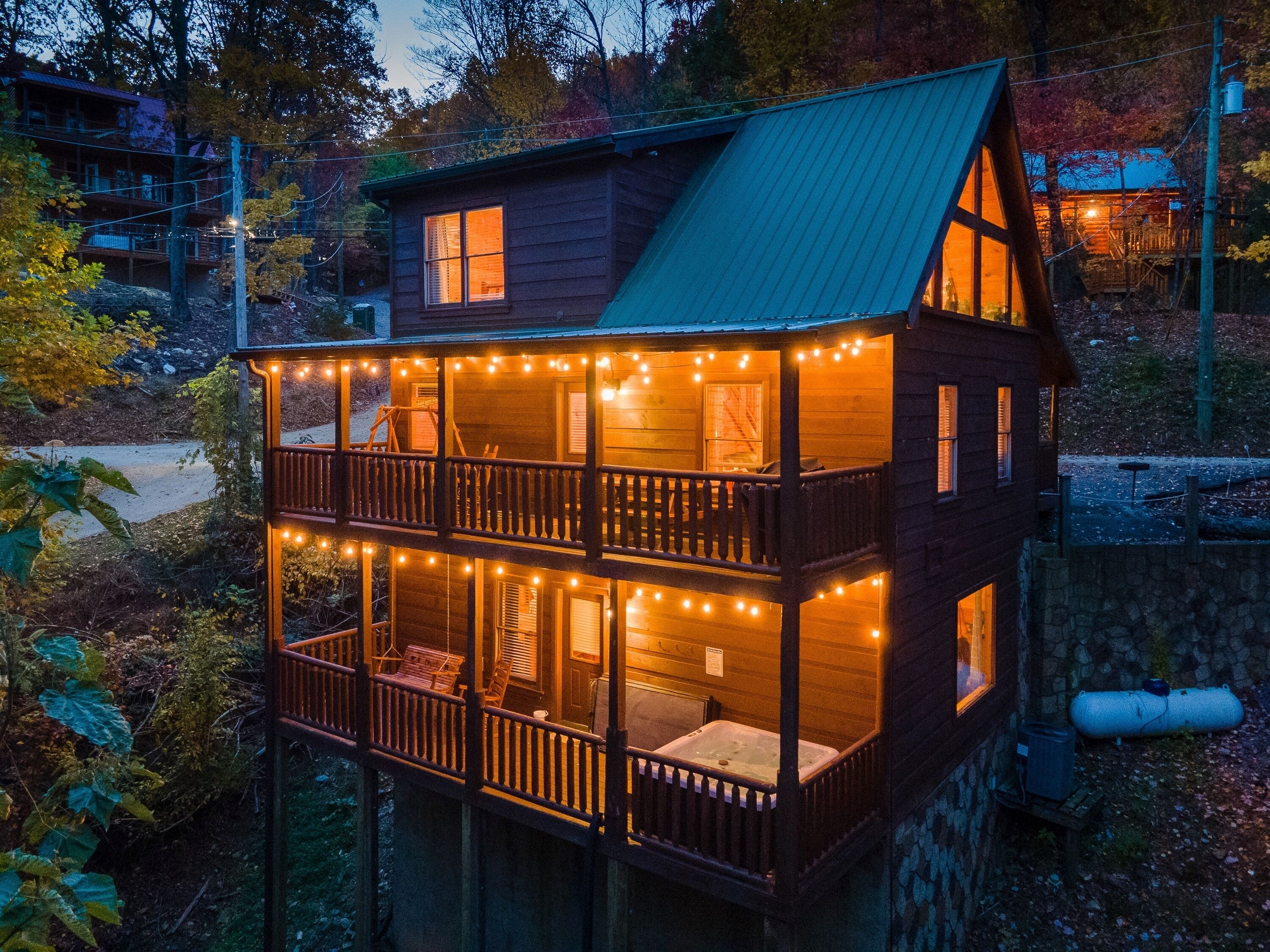 A two-story wooden cabin with a balcony, string lights, and a stone foundation.