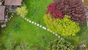 Vista aérea de un jardín ajardinado con un sendero de piedra, árboles de diversos colores y un edificio con techo plano.