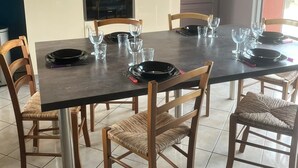 Un coin repas avec une table dressée pour six personnes, entourée de six chaises, et un espace cuisine équipé d’appareils électroménagers et de meubles de rangement.
