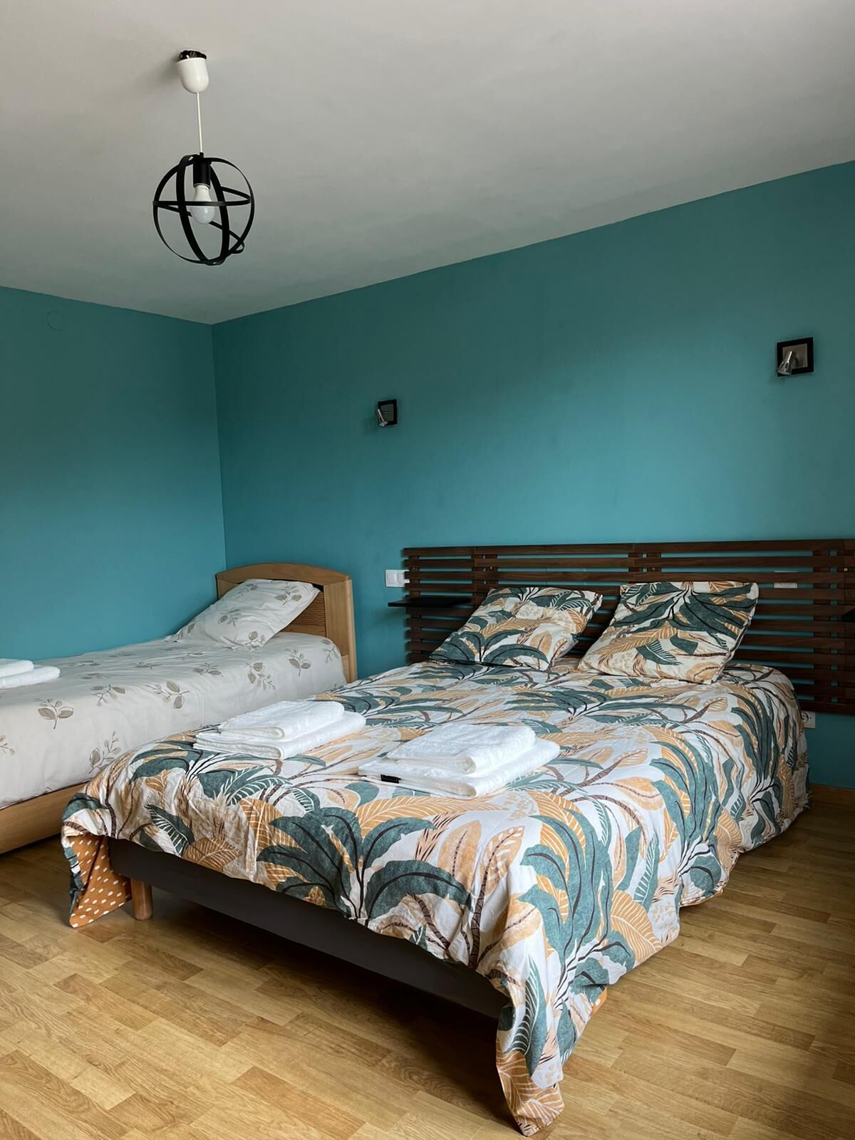Ein Schlafzimmer mit einem Bett, einem Einzelbett, Holzboden und einer Pendelleuchte.