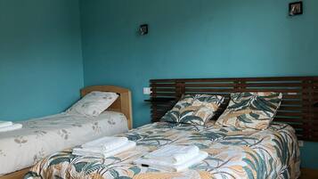 Une chambre à coucher avec un lit, un plus petit lit, un plancher en bois et un luminaire suspendu.