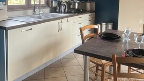Une cuisine moderne dotée d’un grand îlot central, d’un coin repas avec des chaises en bois et offrant une vue sur l’extérieur par la fenêtre.