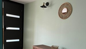 Une pièce avec un meuble en bois, une porte noire dotée de poignées blanches, un luminaire fixé au mur et un élément décoratif mural en fibres tressées.