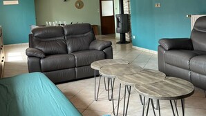 Un salon comprenant un canapé, deux fauteuils et une table basse. On y trouve également une cheminée, une horloge et une porte qui donne sur une autre pièce.
