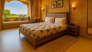 A spacious bedroom with a large bed, a view through a window, and a ceiling fan. - Hotel Grand Haveli Jaisalmer (Jaisalmer)