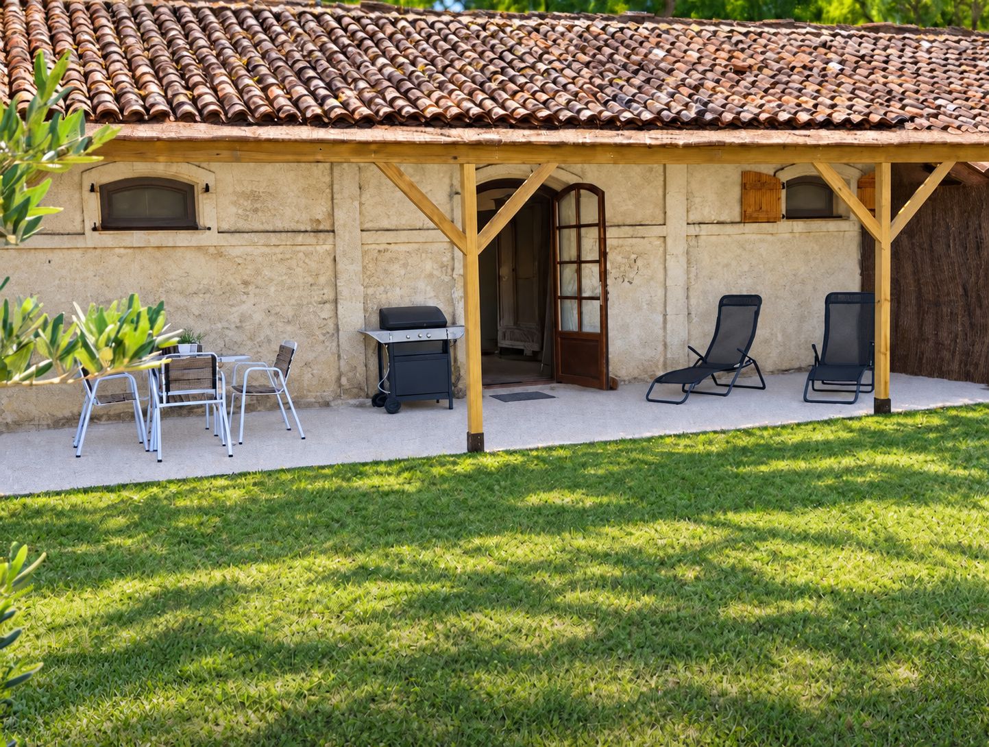 A covered patio area with a grill, outdoor seating, and a view of a building with a tiled roof.