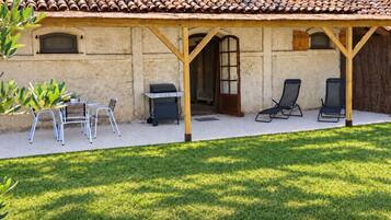 A covered patio area with a grill, outdoor seating, and a view of a building with a tiled roof.