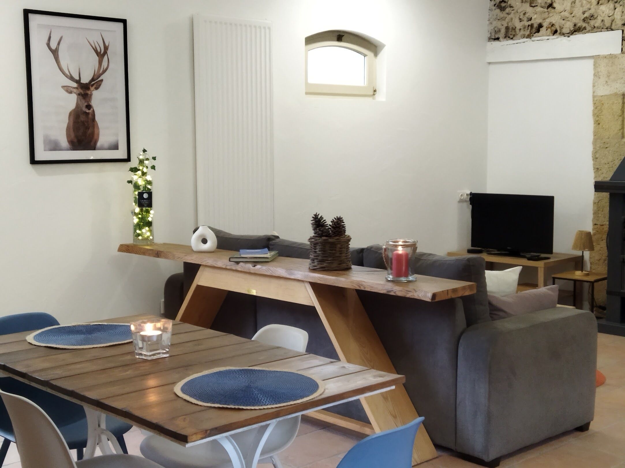 A modern living room with a wooden dining table, blue chairs, a grey sofa, a TV, and a fireplace.