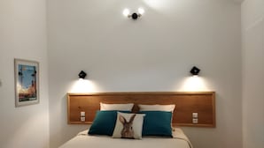Un lit bien fait, avec une tête de lit en bois, deux lampes fixées au mur et un tableau encadré accroché au mur.