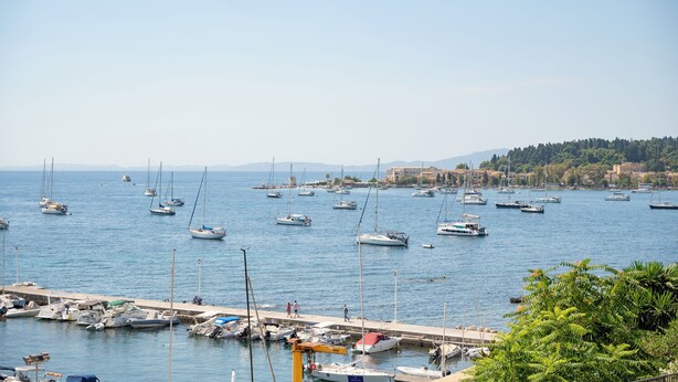 A marina with numerous boats docked, a pier, and a backdrop of hills and buildings. - Joseph's Studio by Corfuescapes (Corfu)
