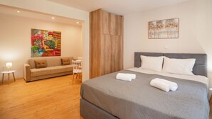 A modern hotel room with a large bed, a sofa, a small table, and artwork on the walls. - Joseph's Studio by Corfuescapes (Corfu)