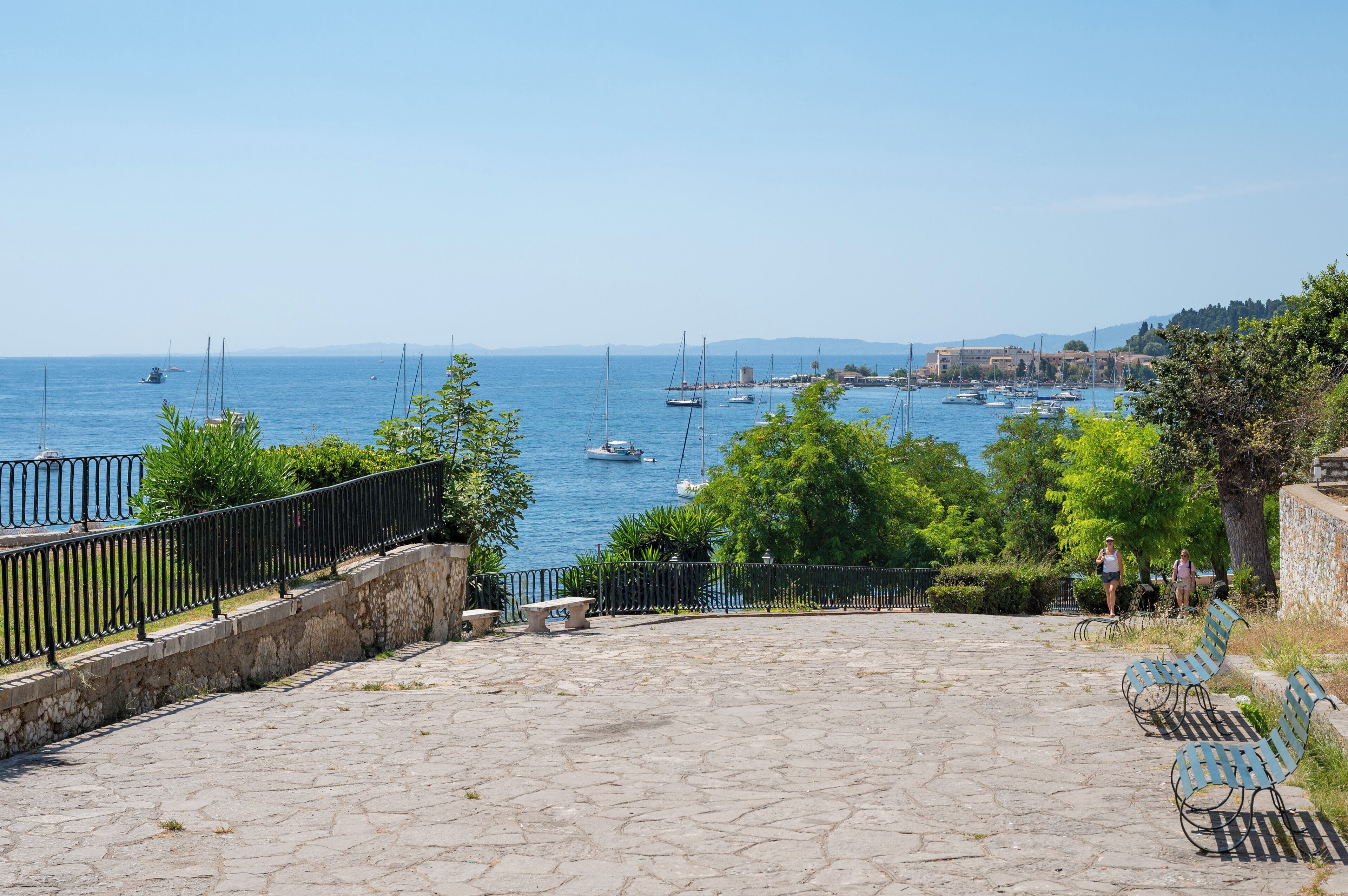 Un passeig de pedra amb vistes a una marina plena de vaixells i una ciutat a la distància.