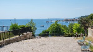 A stone-paved promenade overlooking a marina with boats and a distant town. - Joseph's Studio by Corfuescapes (Corfu)