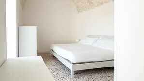 Een slaapkamer met een bed, een witte nachtkastje en een witte lamp.