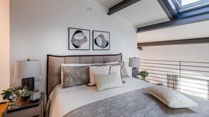 A modern bedroom with a large bed, two wall-mounted abstract art pieces, a skylight, and a balcony with a railing. - Verdi 1928, A Cozy Wallside Retreat (Lucca)