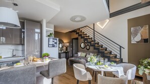 A modern kitchen with a marble countertop, a dining area with a round table and chairs, and a staircase with a black railing. - Verdi 1928, A Cozy Wallside Retreat (Lucca)