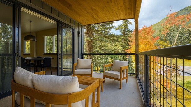 Un balcone con mobili in legno, un'area pranzo e vista su alberi autunnali.
