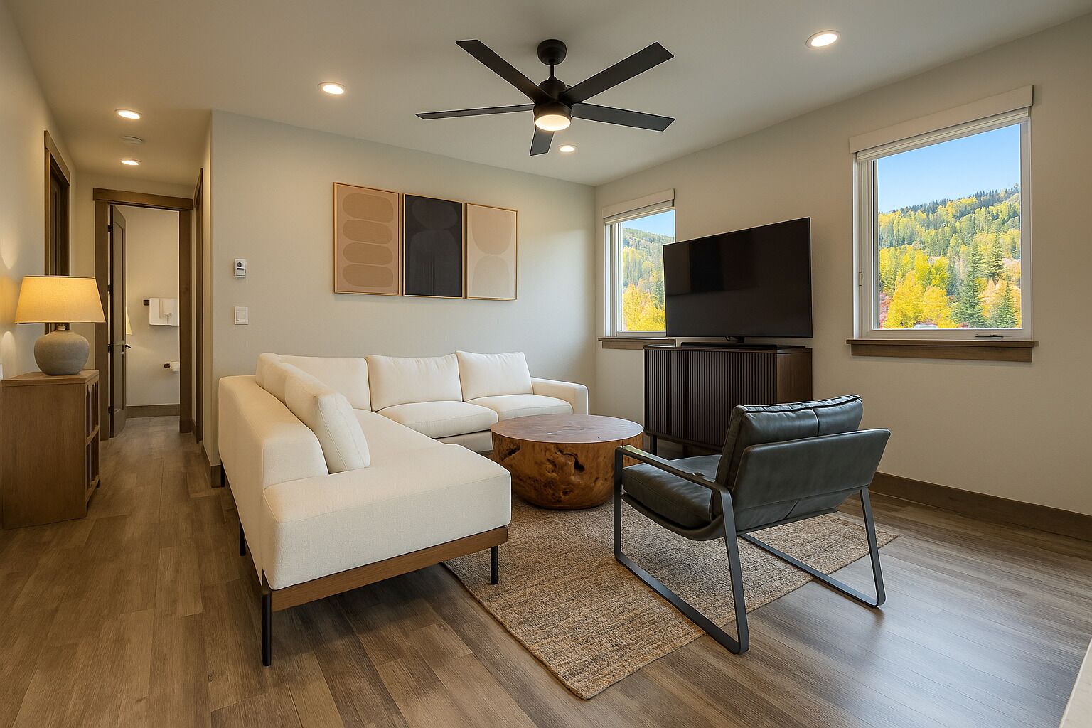 A modern living room with a sectional sofa, a round coffee table, a leather chair, a flat-screen TV, and a ceiling fan.