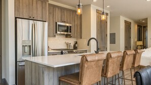 Una cucina moderna con mobili in legno, elettrodomestici in acciaio inossidabile e un'isola centrale con sgabelli da bar.
