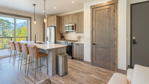 Una cucina moderna con isola centrale, sgabelli da bar, un cestino in acciaio inossidabile e un'ampia porta in legno.