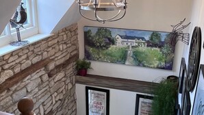 Un escalier avec un mur en pierre, un lustre et des œuvres d’art encadrées.
