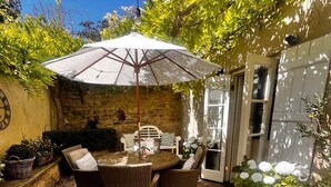 Une terrasse avec une table ronde et des chaises, un grand parasol et des plantes en pot.