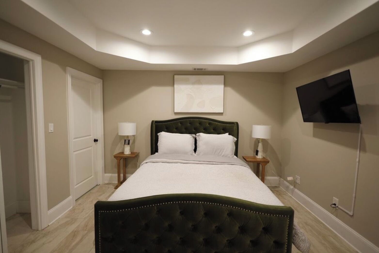 A bedroom with a bed, two bedside tables, a flat-screen TV, and a door.
