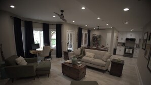 A spacious living room with a sofa, armchairs, and a coffee table. There is a dining area with a table and chairs, and a kitchen with cabinets and appliances. - Eclectic Charm (Douglasville)