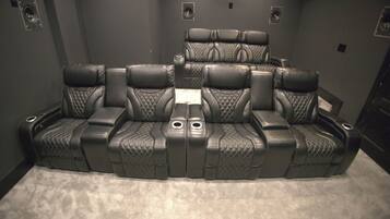A home theater room with a curved black leather couch, a central console, and wall-mounted speakers.