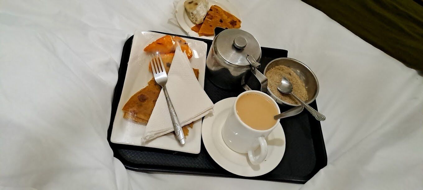 Uma bandeja com um prato de comida, uma xícara de café e um açucareiro sobre uma cama.