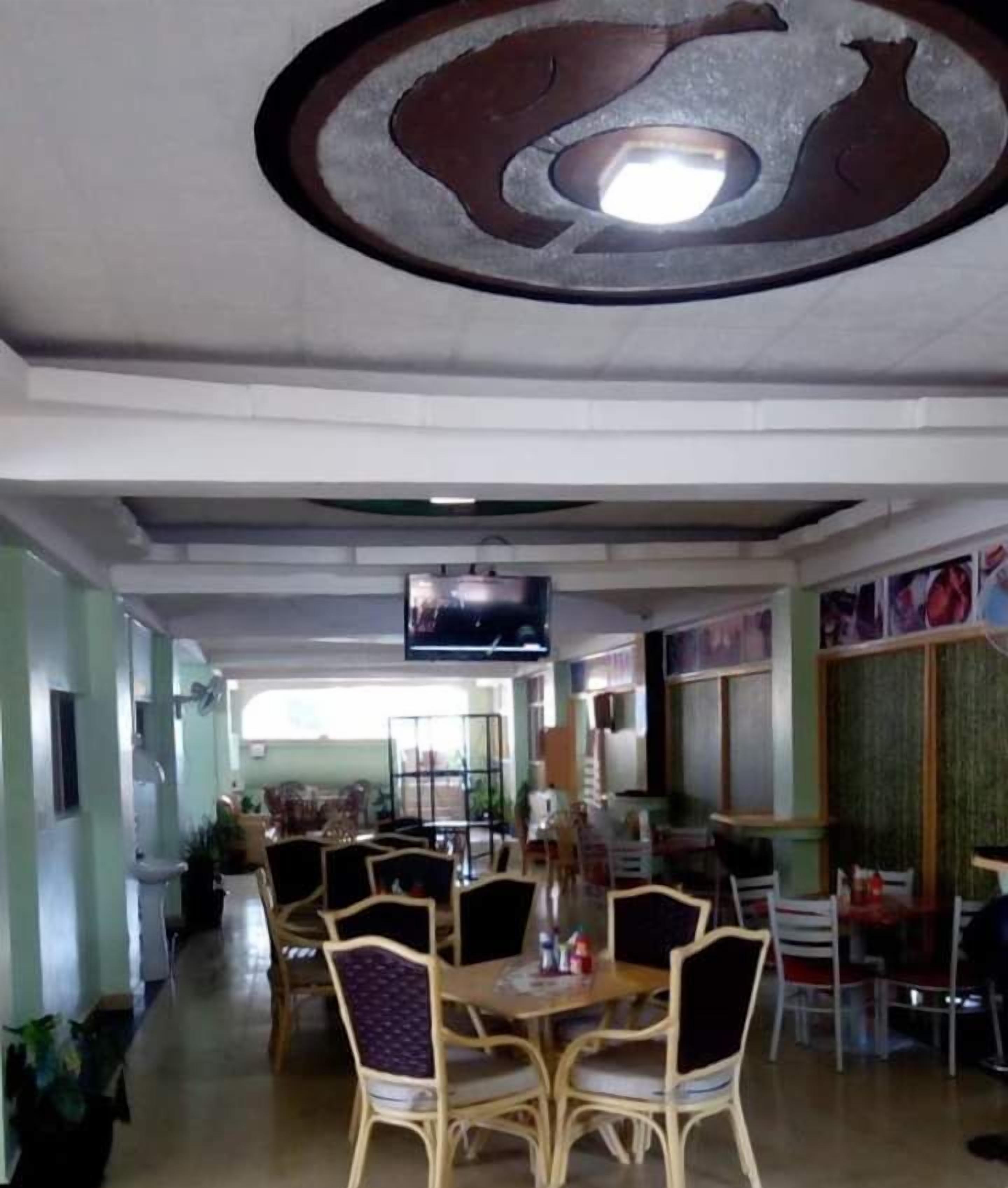 Un ristorante con sala centrale caratterizzata da tavoli e sedie rotonde, un soffitto a motivi circolari e uno schermo televisivo.