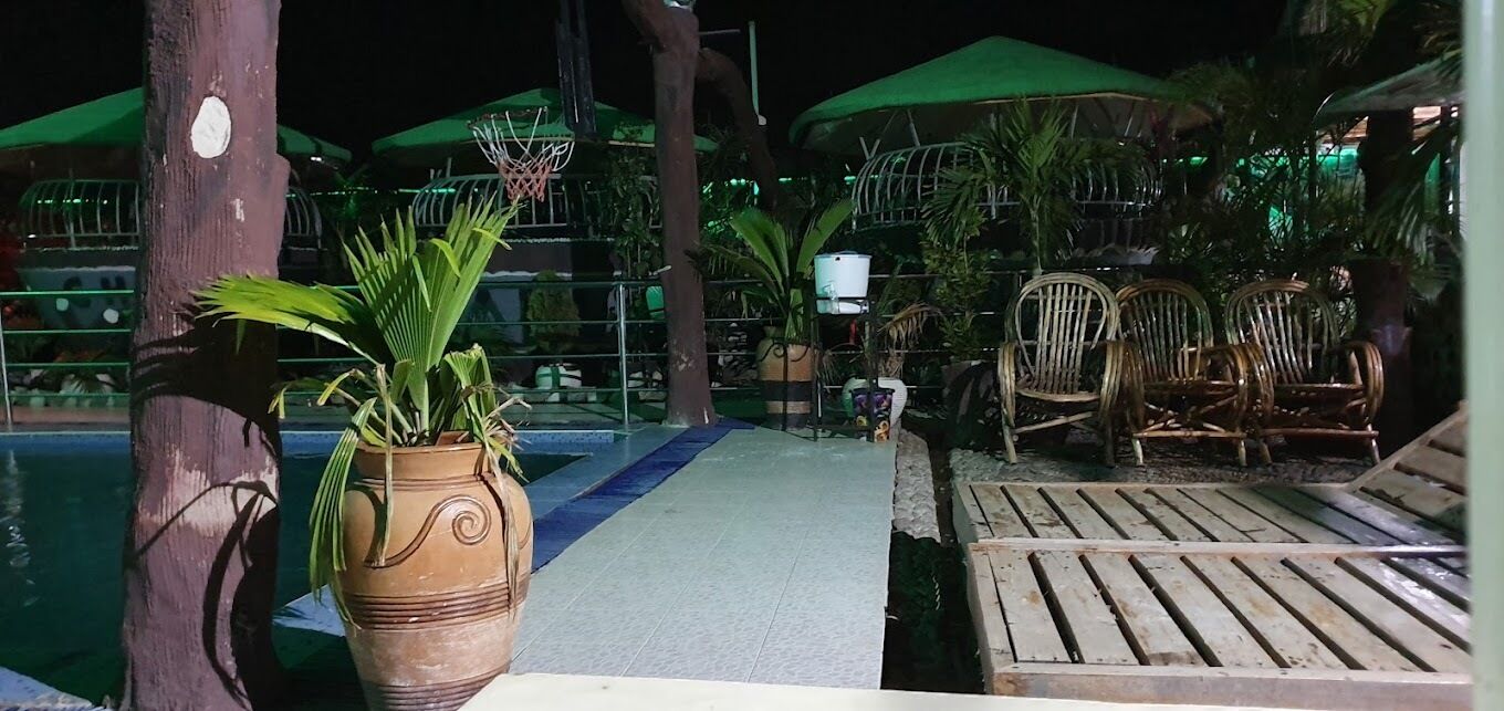 A poolside area with a wooden bench, wicker chairs, and a potted plant.