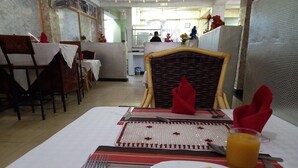 Un coin repas avec une table dressée pour deux personnes, comprenant une assiette de nourriture et un verre de jus d’orange.