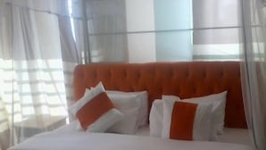 Un lit bien fait, avec une literie blanche et orange, une serviette enroulée et une tête de lit orange à motifs.