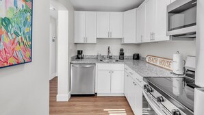 Une cuisine moderne avec des meubles blancs, un lave-vaisselle en acier inoxydable, un plan de travail en granit et une cuisinière.