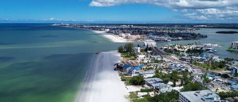 An aerial view of a coastal town with a beach, residential buildings, and a marina.