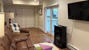 Ein Wohnzimmer mit einer braunen Ledersofa, einem schwarzen Kamin, einem an der Wand montierten Fernseher und einer Tür, die auf einen Balkon führt.