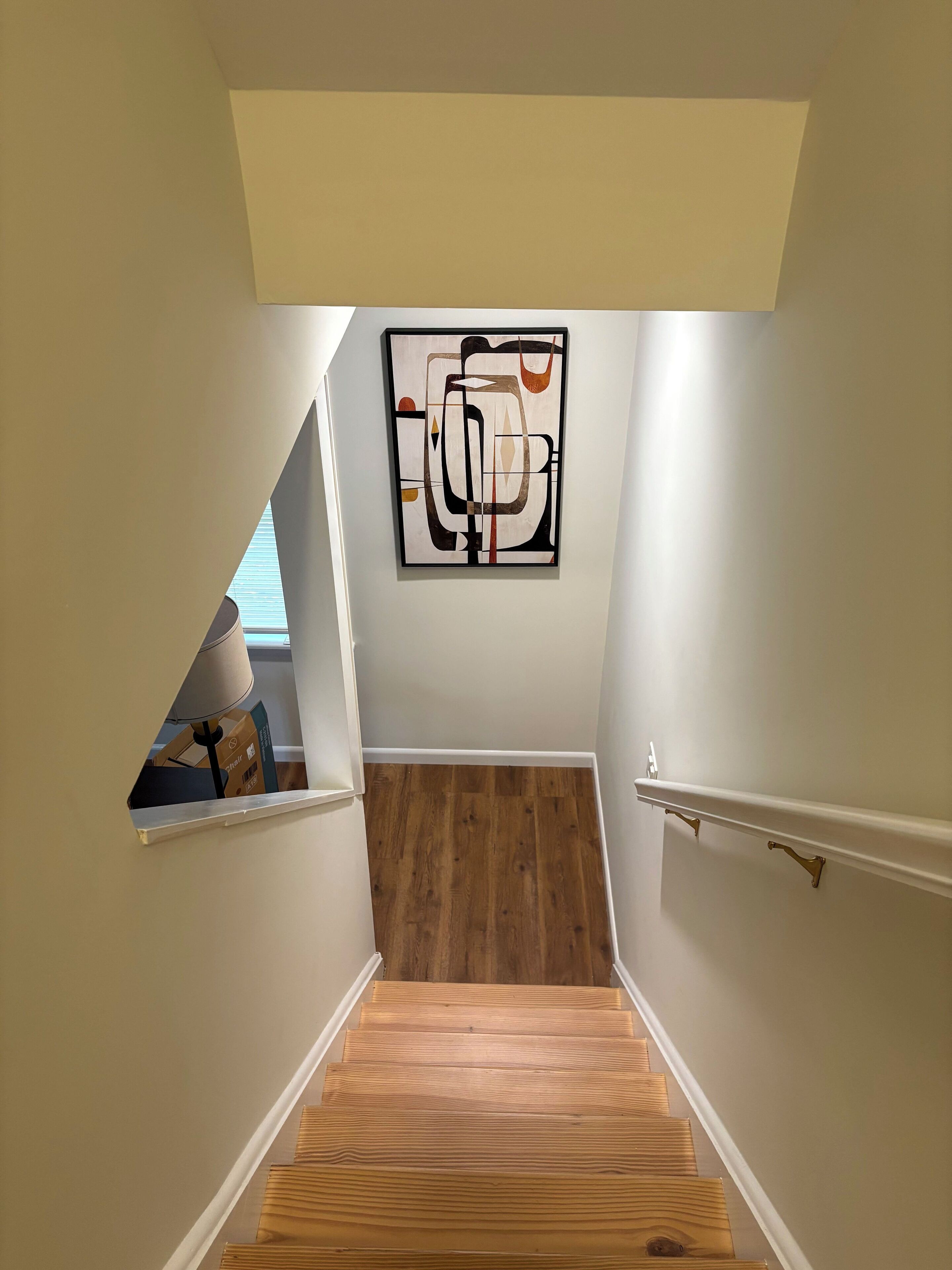 A staircase with wooden steps and a white wall. A framed abstract artwork hangs on the wall above the stairs.