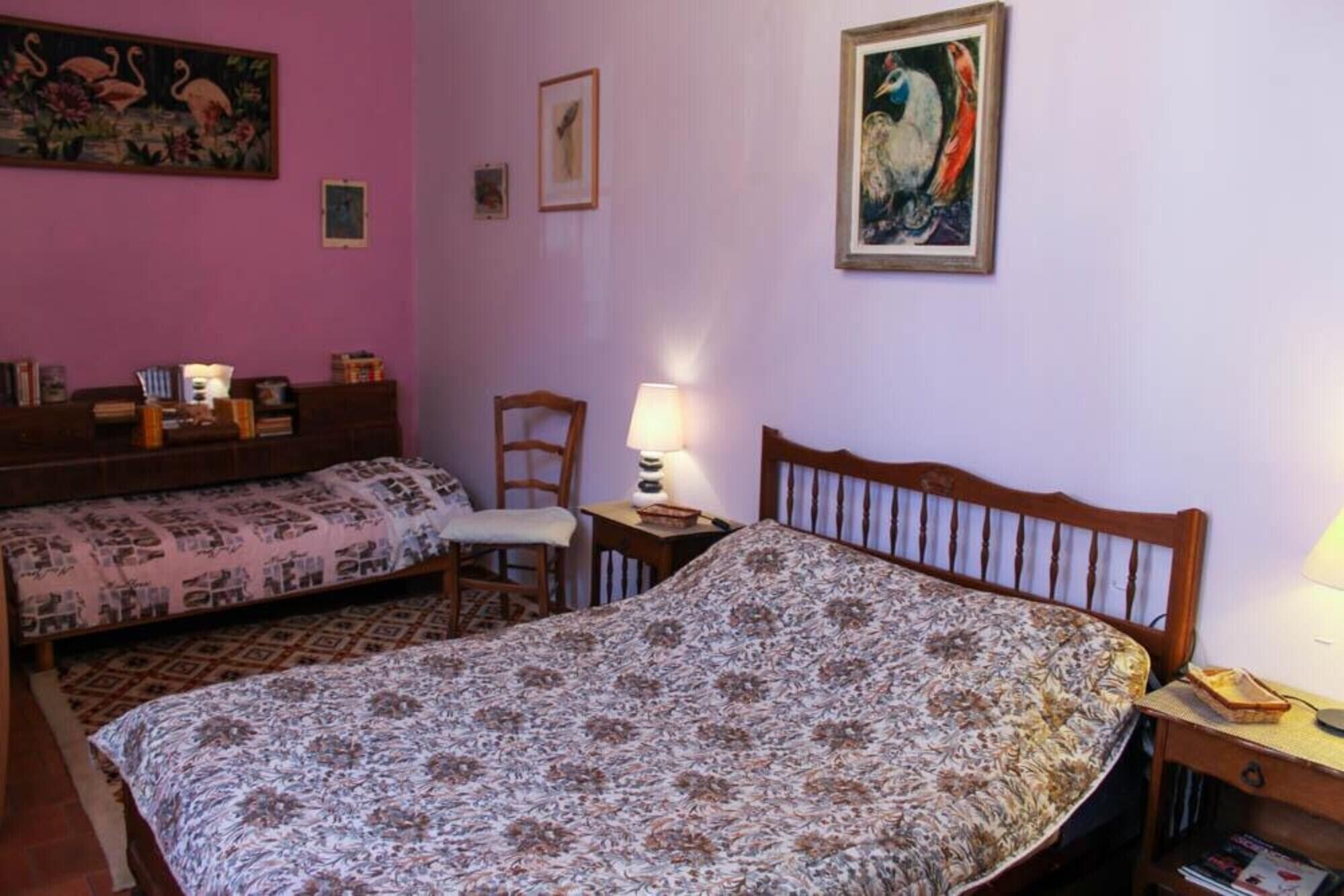 A bedroom with two beds, a chair, a nightstand, and a wall with framed artwork.