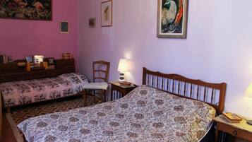 A bedroom with two beds, a chair, a nightstand, and a wall with framed artwork.