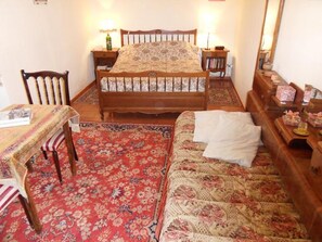 A bedroom with a bed, two bedside tables, a chair, a small table, and a mirror.