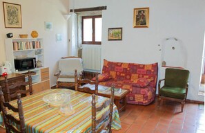 Una sala de estar con sofá, una silla, una mesa de comedor con sillas, una estantería y un televisor.