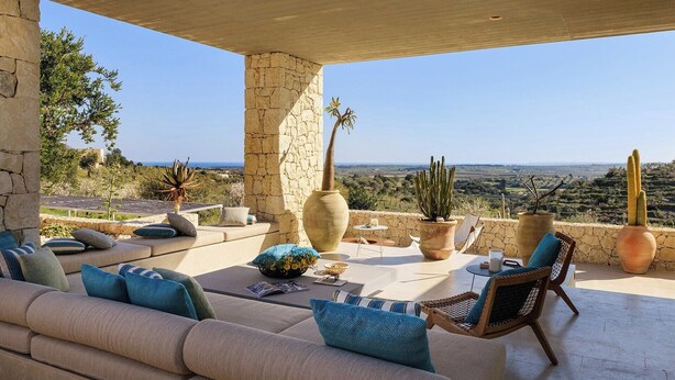 Un espacio de estar al aire libre cubierto con pared de piedra, un sofá, sillas y macetas grandes con cactus.