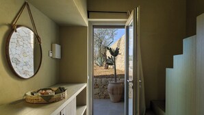 Un pasillo estrecho con pared de piedra, una encimera de madera y una cesta tejida, y vistas de un cactus al exterior.