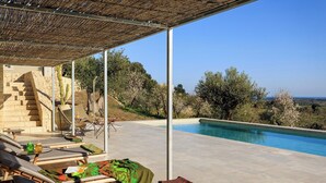 Zona junto a la piscina con sillones, una mesa con una bebida y vistas a la piscina y al paisaje.