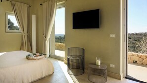 Un dormitorio con cama, televisión, ventana con cortinas y vistas al exterior.
