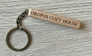 A wooden keychain with the inscription "OROPOS COZY HOUSE" on a textured surface. - Cozy, bright home near to the nature for calm moments. (Nea Palatia)