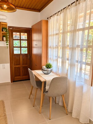 A dining area with a wooden table, two chairs, a potted plant, and a window with sheer curtains. - Cozy, bright home near to the nature for calm moments. (Nea Palatia)