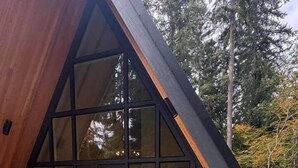Una cabaña de madera moderna con un jacuzzi en primer plano y un ventanal que da a un patio.